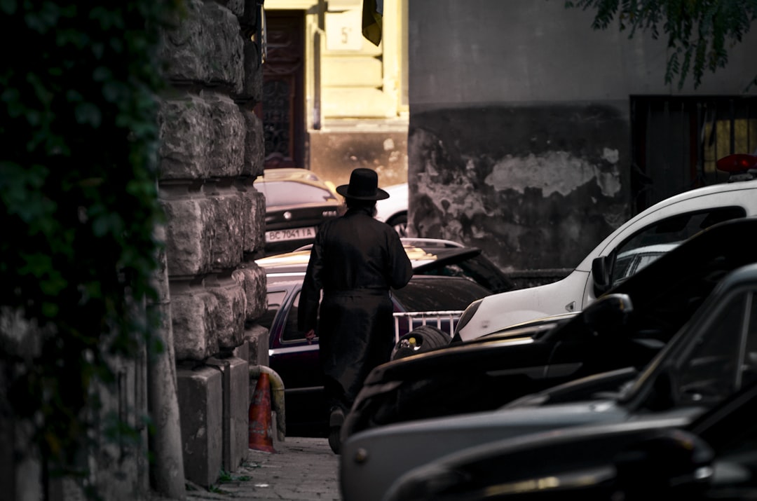 man in black jacket and brown hat standing beside black car during daytime