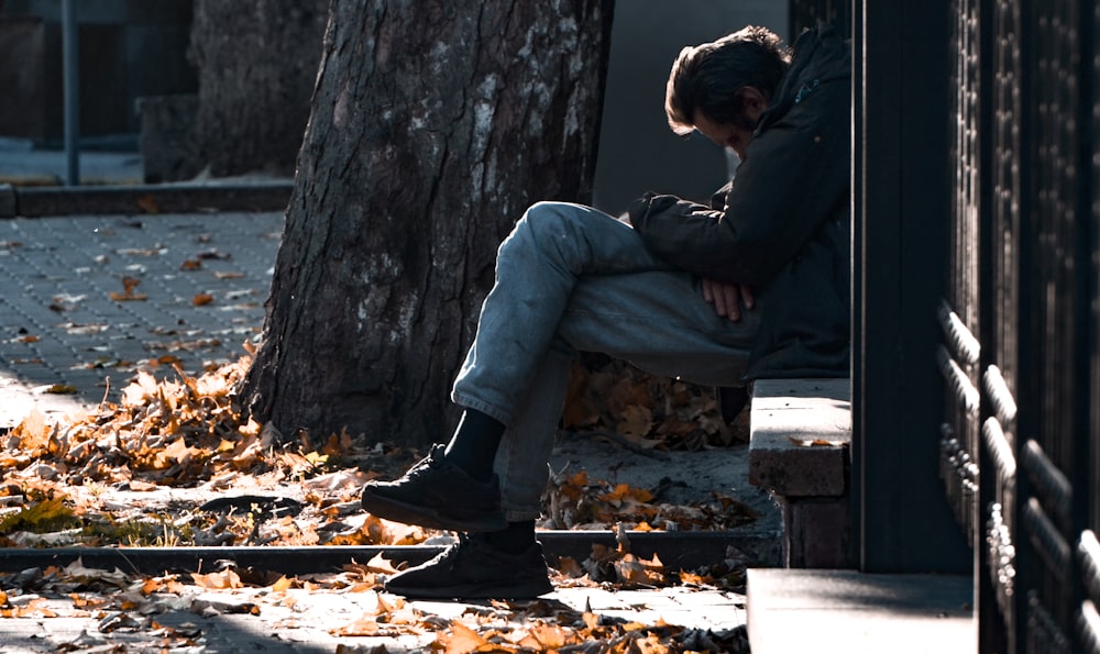 man in black jacket and blue denim jeans sitting on brown wooden bench