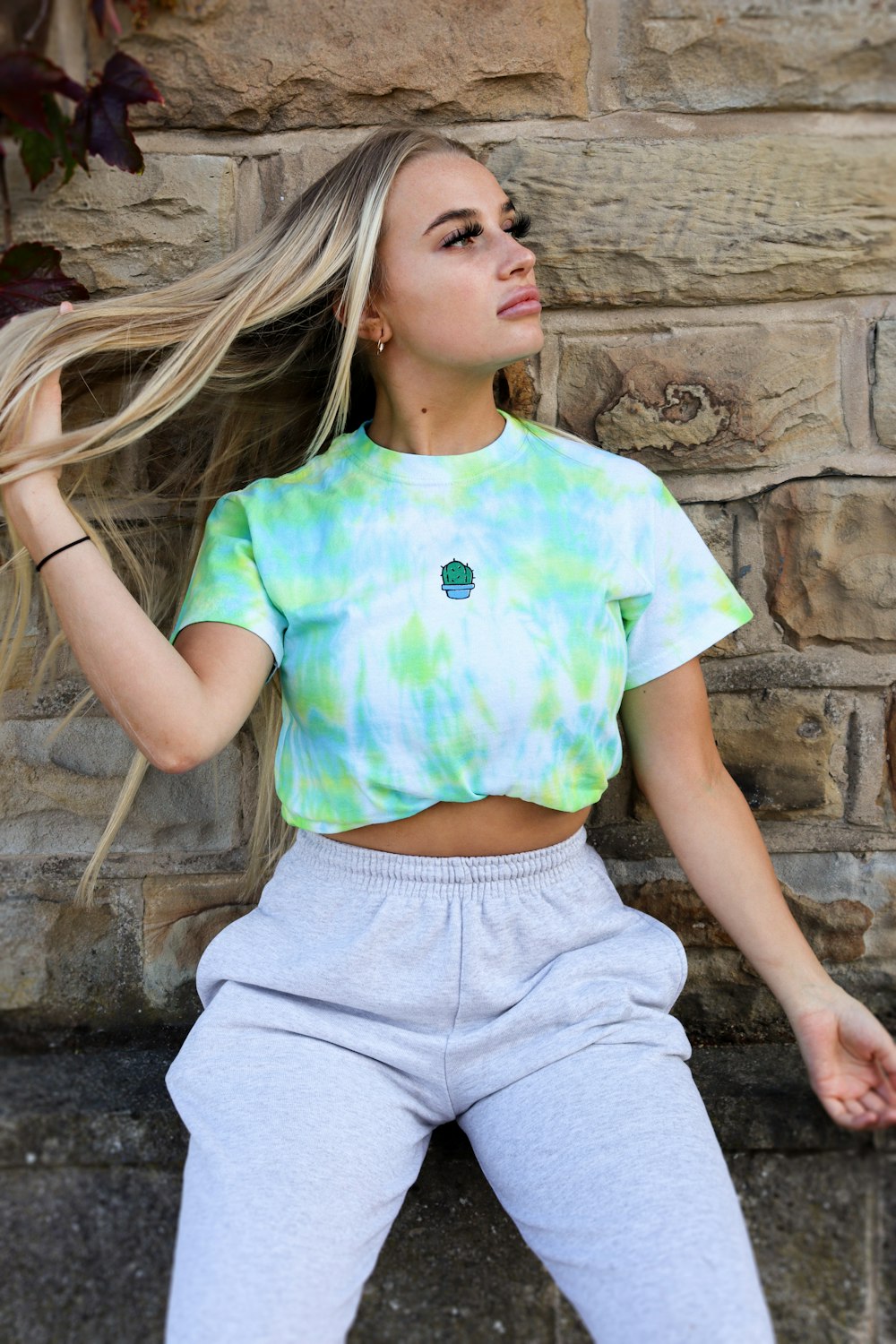 woman in green crew neck t-shirt and gray denim shorts sitting on brown concrete wall