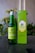 A green bottle labeled 'Hijau Buru Minyak Kayu Putih' is placed next to a matching green box with yellow and green striped design. The background features blurred green foliage.