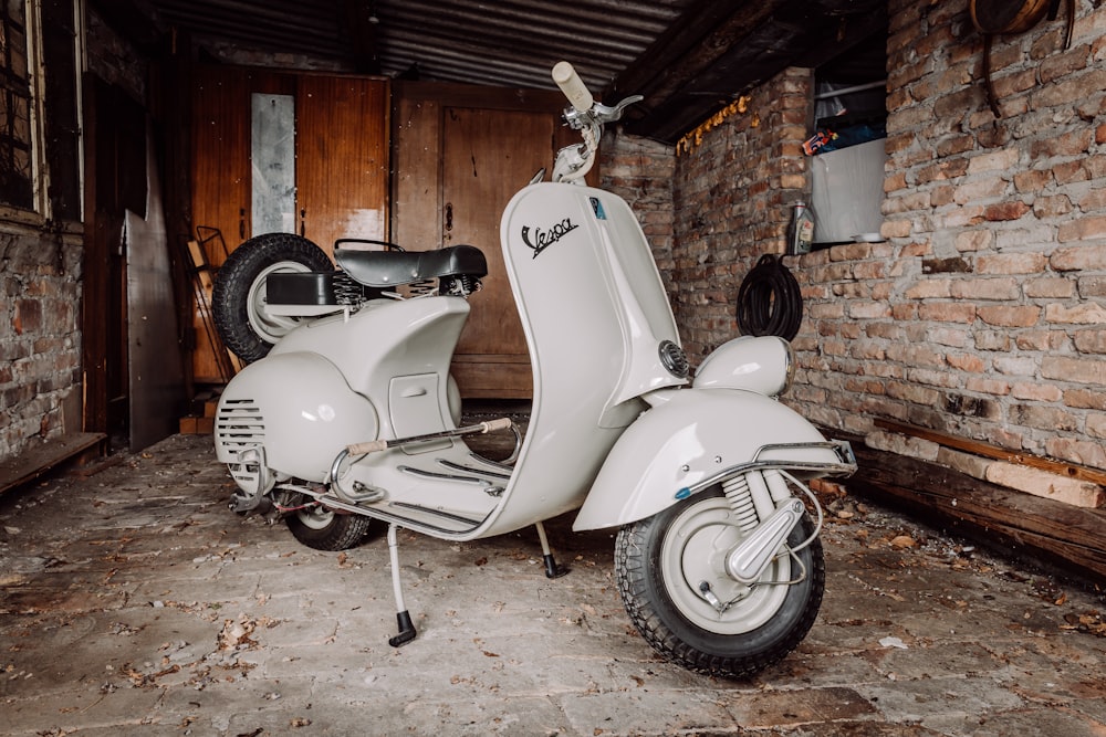 white and black motor scooter parked beside brown brick wall