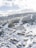 A snow-covered mountain resort featuring numerous wooden chalets nestled among alpine trees. The landscape is dominated by the vast, rolling mountains in the background, offering a picturesque winter scene. Winding roads connect the buildings, with ski tracks visible on the slopes.