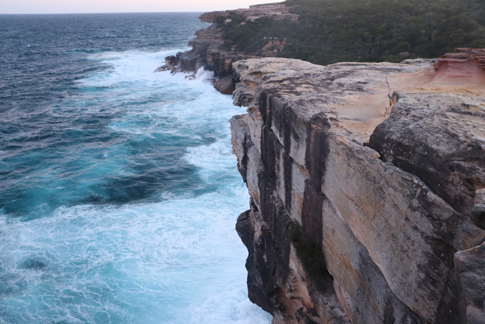 brown rocky mountain beside blue sea during daytime