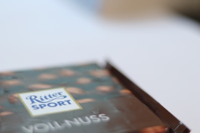 A blurred image focusing on a chocolate packaging with the words 'Ritter Sport' and 'Voll-Nuss' visible. The packaging design includes a pattern of nuts on a dark background.