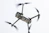 A drone captured in flight against a light sky background. The focus is on the body and propellers, with rotors in motion creating a blur effect. The drone appears sleek and modern, featuring sensors and a camera on the front.