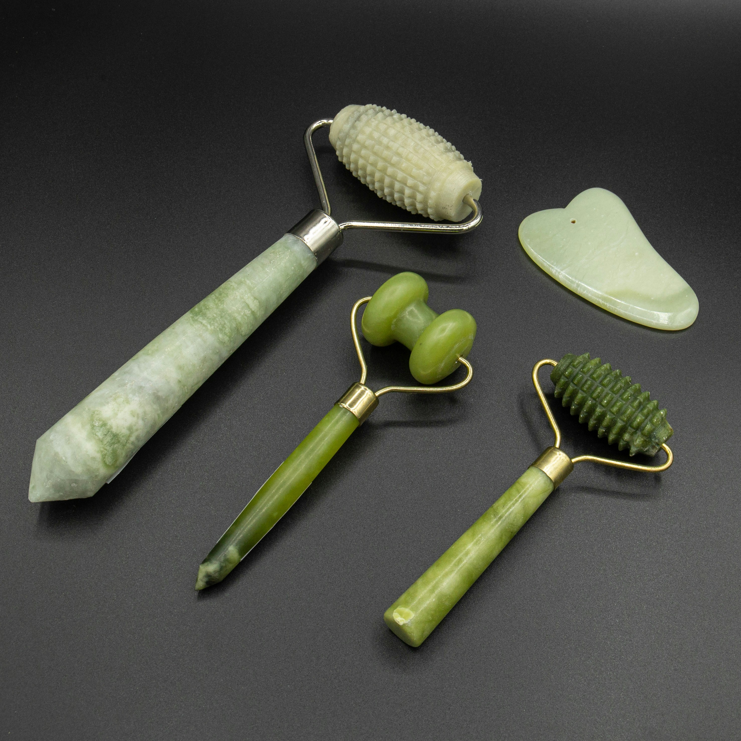 Green jade gua sha facial tool on white ceramic dish with white rose petals, spa aesthetic