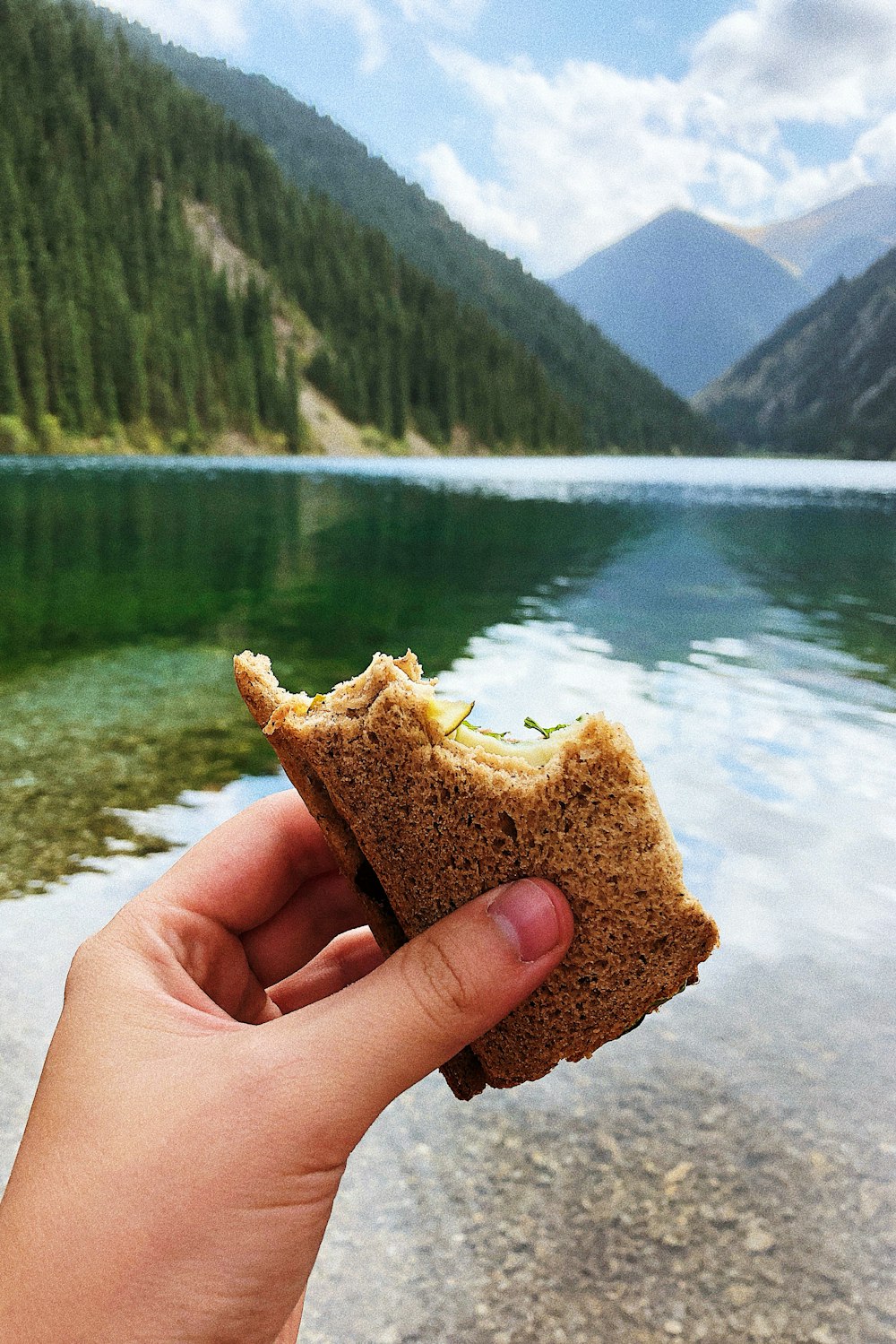 a hand holding a piece of bread over a lake