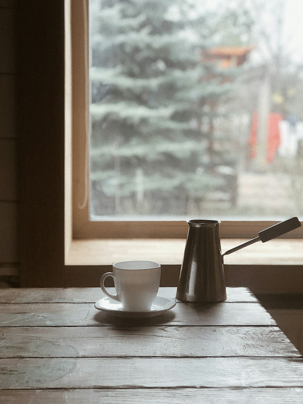 white ceramic mug on saucer beside silver steel pitcher