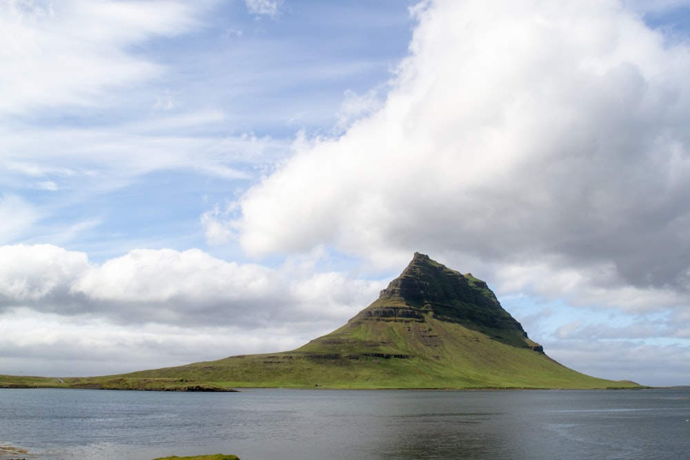 green mountain beside body of water under white clouds during daytime