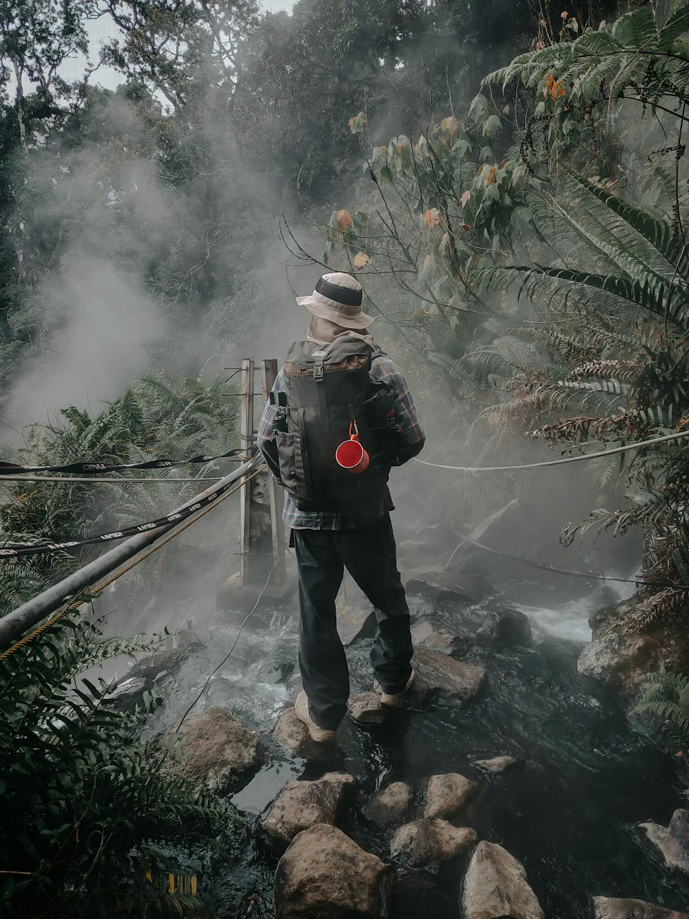 man in black jacket and blue denim jeans standing on brown wooden bridge