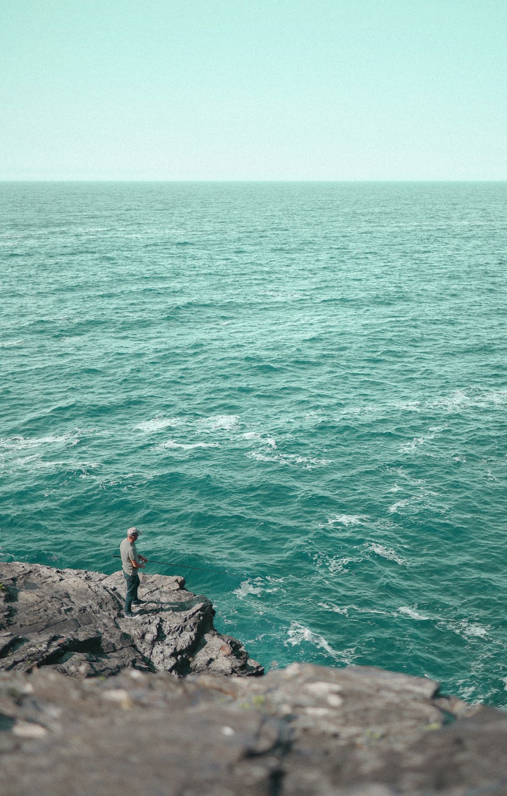 person in black shirt sitting on rock near body of water during daytime