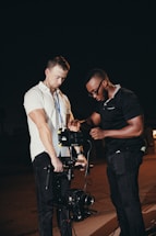 Two individuals are focused on setting up a professional camera rig at night. They are adjusting equipment, suggesting collaboration and technical engagement.