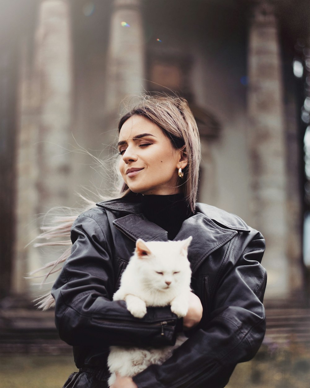 girl in black leather jacket holding white cat