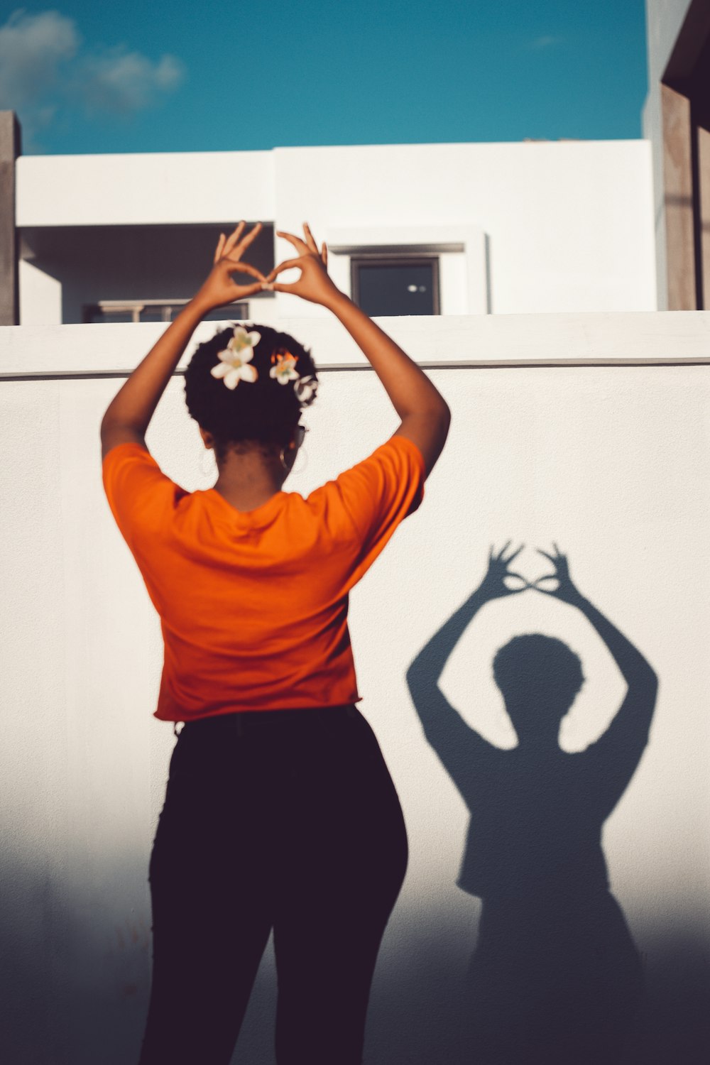 woman in orange shirt and black skirt standing and raising both hands