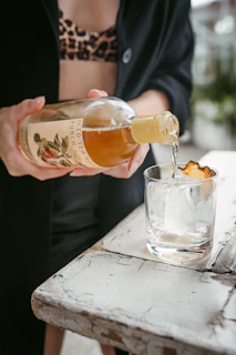 person pouring brown liquid on clear drinking glass