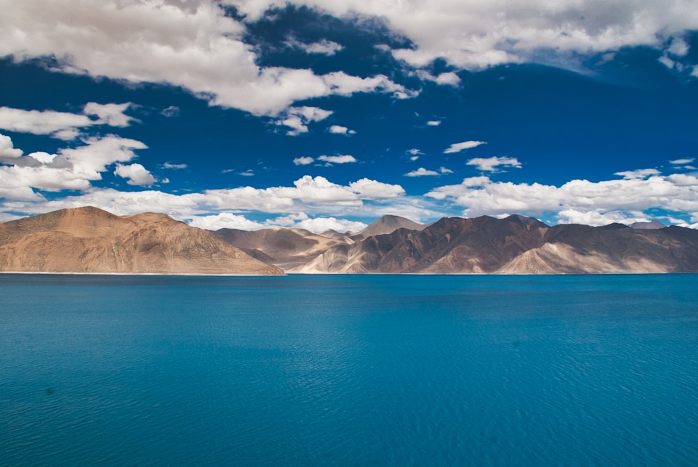 blue sea near brown and white mountains under blue sky during daytime