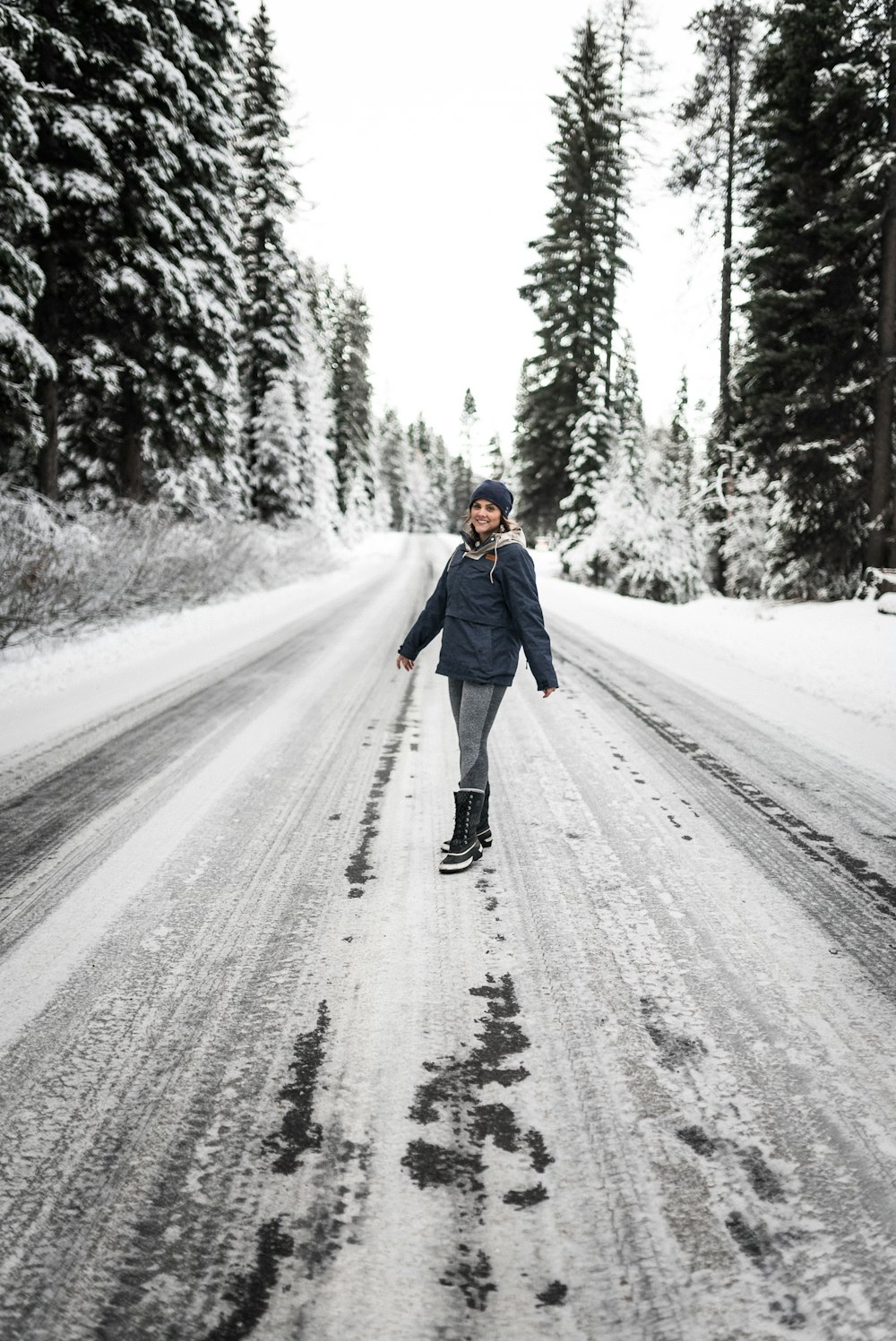 woman in blue coat walking on snow covered road during daytime