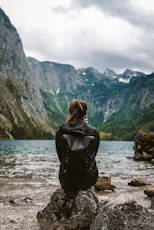 woman in black leather jacket standing on rock near body of water during daytime