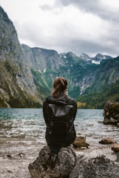 woman in black leather jacket standing on rock near body of water during daytime