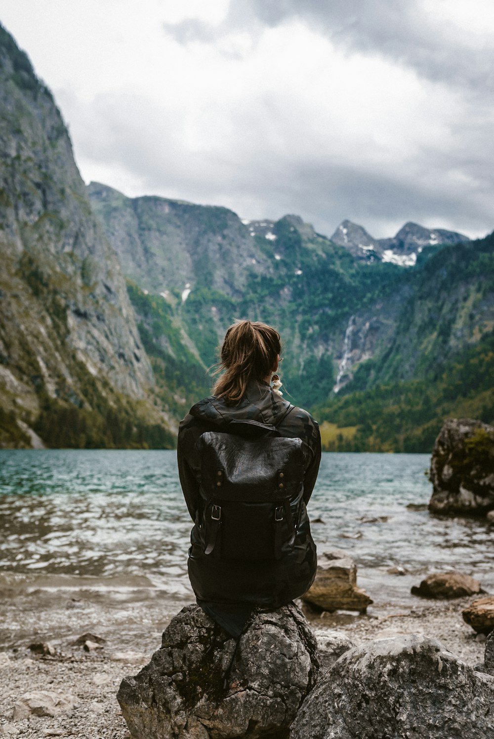 mulher na jaqueta de couro preta de pé na rocha perto do corpo de água durante o dia