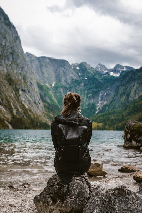woman in black leather jacket standing on rock near body of water during daytime in Berchtesgaden National Park Germany