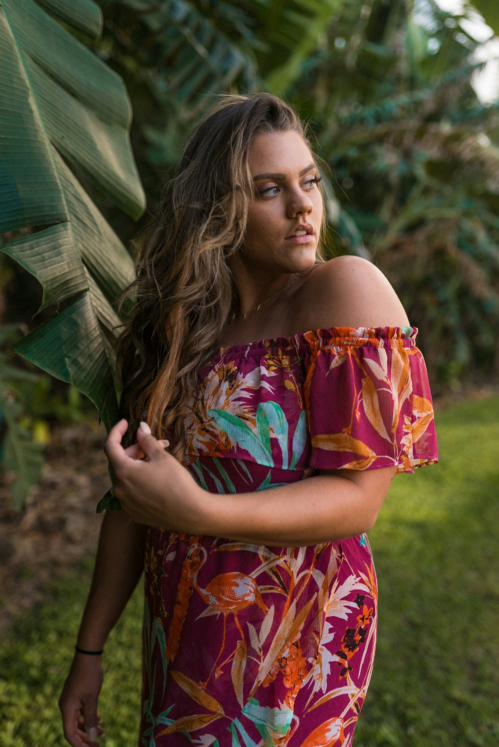 woman in red blue and yellow floral off shoulder dress holding green umbrella