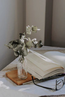 An intimate still life of a worn journal, a cup of tea, and a pair of reading glasses on a sunlit wooden table.