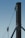 A close-up of a sturdy steel structure featuring a vertical beam with two attached metal cables. One cable is secured with a metal bracket, and the other is connected to a pulley system. The background is a clear blue sky, emphasizing the industrial design.
