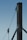 A close-up of a sturdy steel structure featuring a vertical beam with two attached metal cables. One cable is secured with a metal bracket, and the other is connected to a pulley system. The background is a clear blue sky, emphasizing the industrial design.