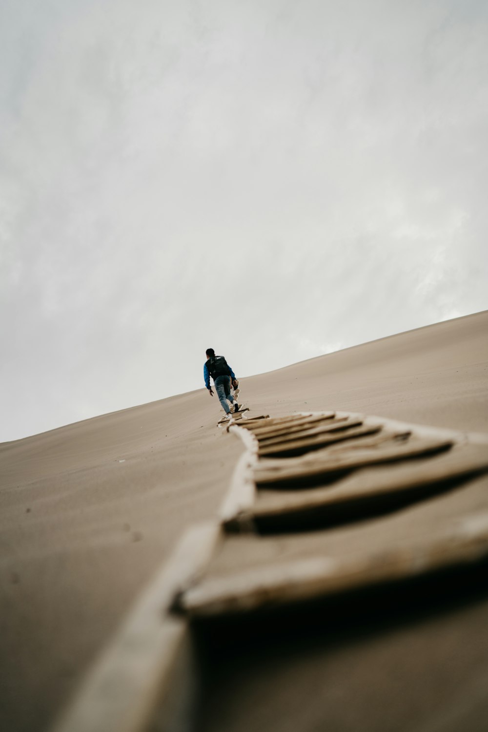 man in black jacket and blue denim jeans walking on brown sand during daytime