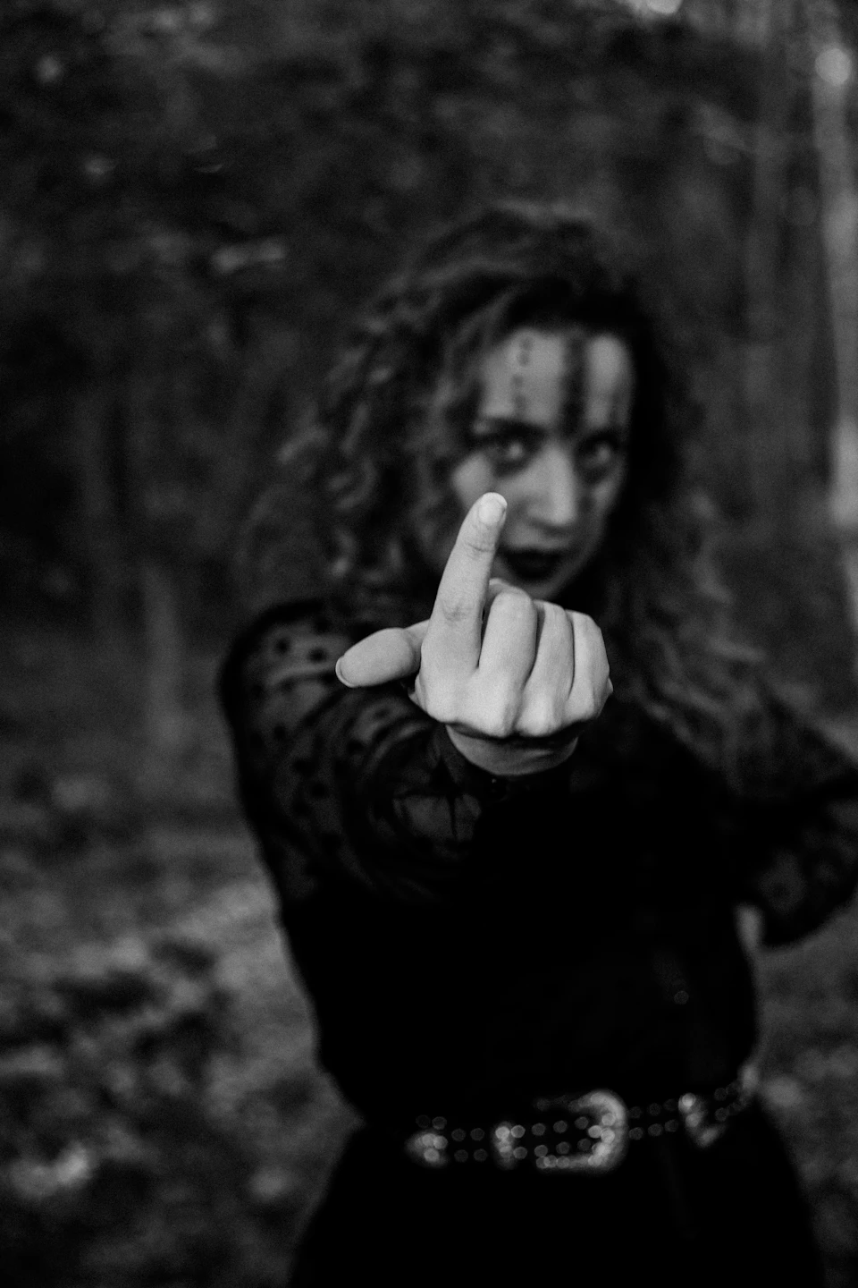 Person makes peace sign with index finger, surrounded by trees and foliage outdoors