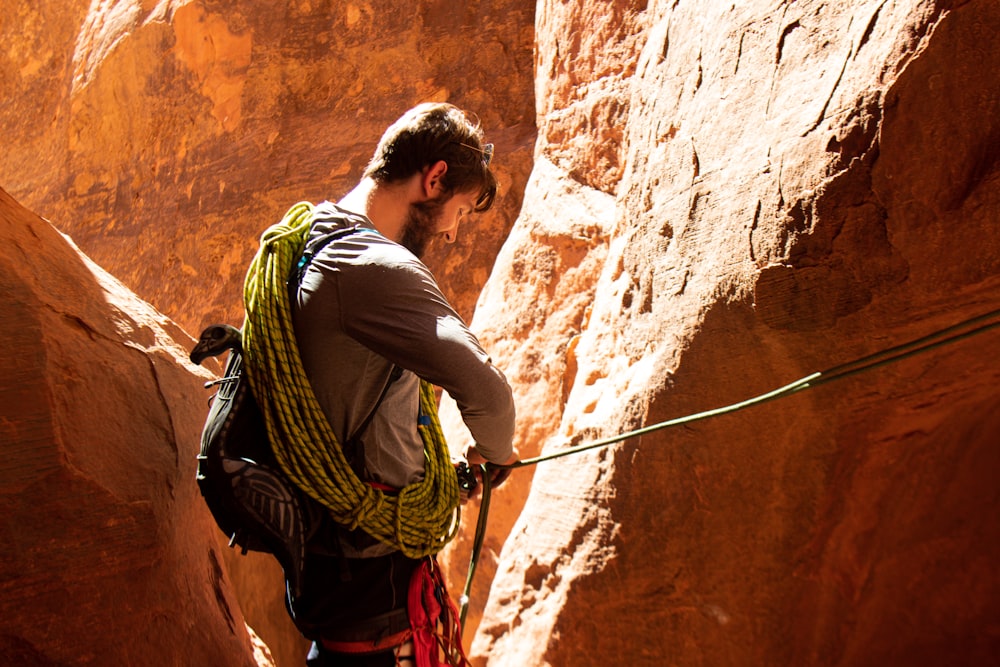 man in white t-shirt and green backpack climbing on brown rock