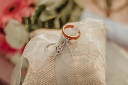 A soft, romantic scene of wedding rings resting atop delicate champagne-hued silk fabric.