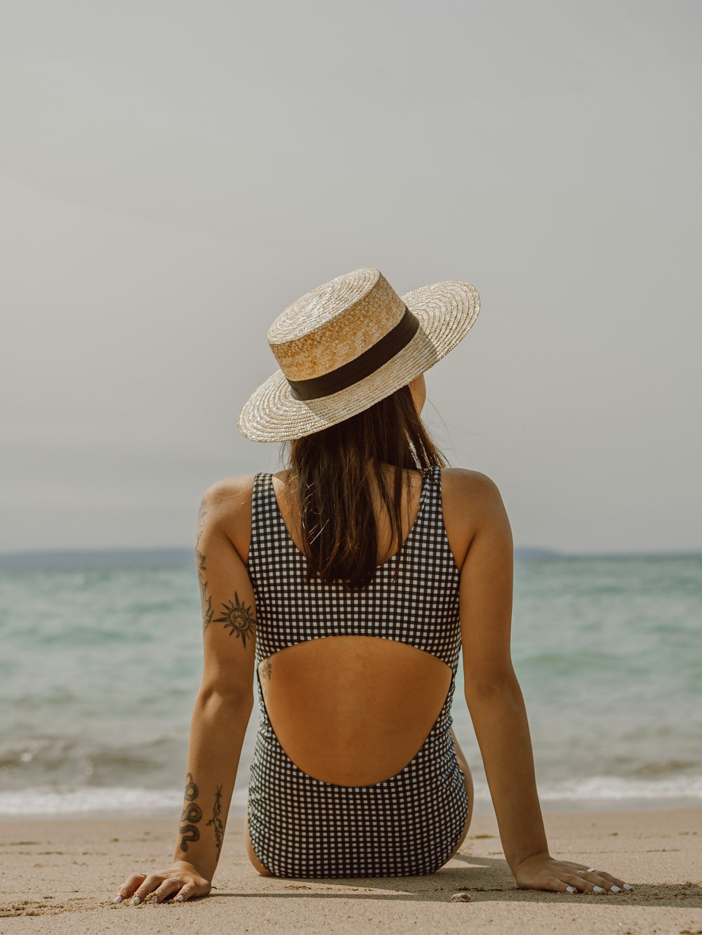 donna in bikini a pois in bianco e nero che indossa un cappello da sole marrone in piedi sulla spiaggia durante