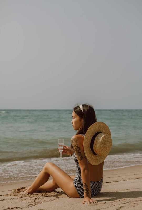 woman in brown sun hat holding clear drinking glass on beach during daytime in Tiny Canada