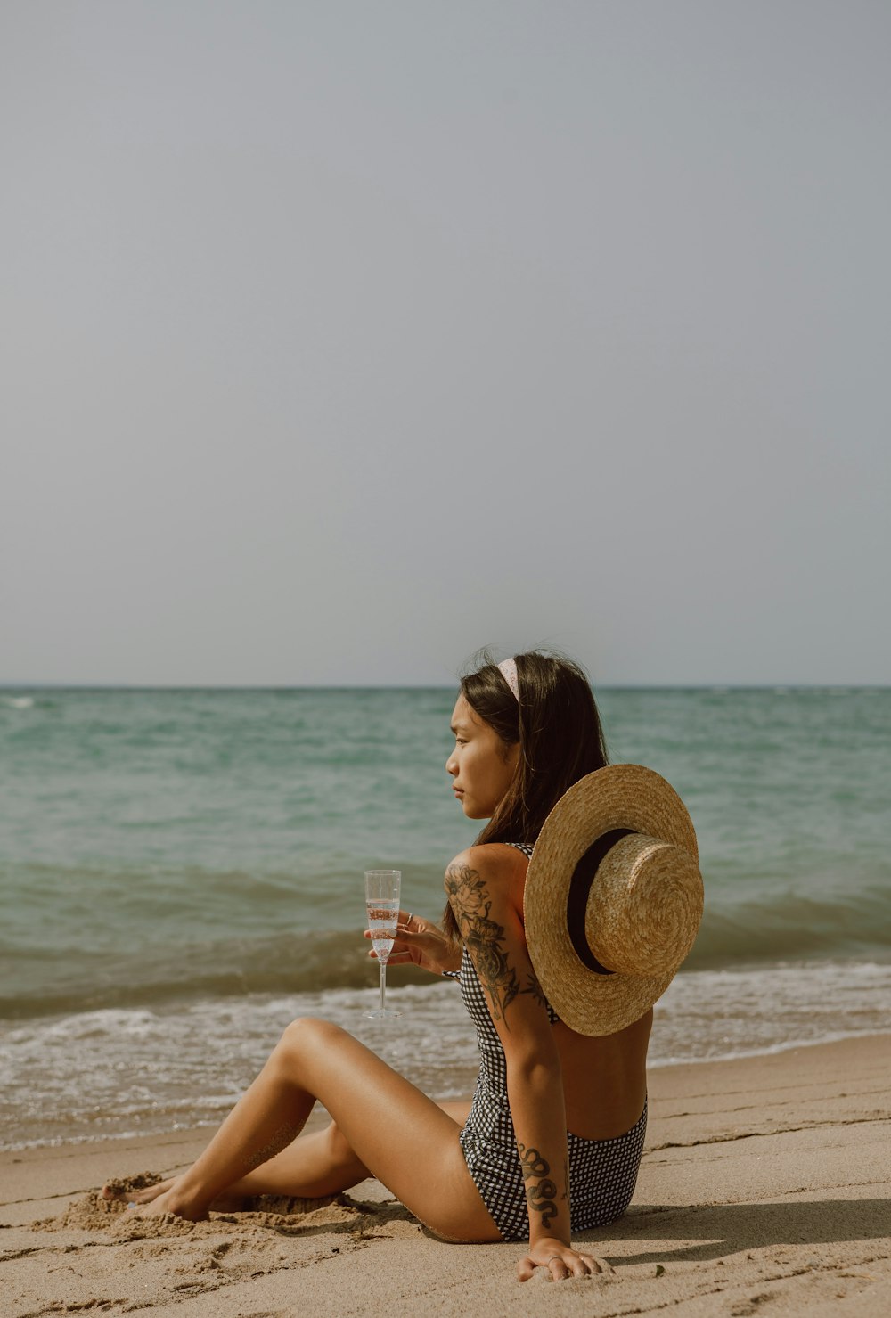 woman in brown sun hat holding clear drinking glass on beach during daytime