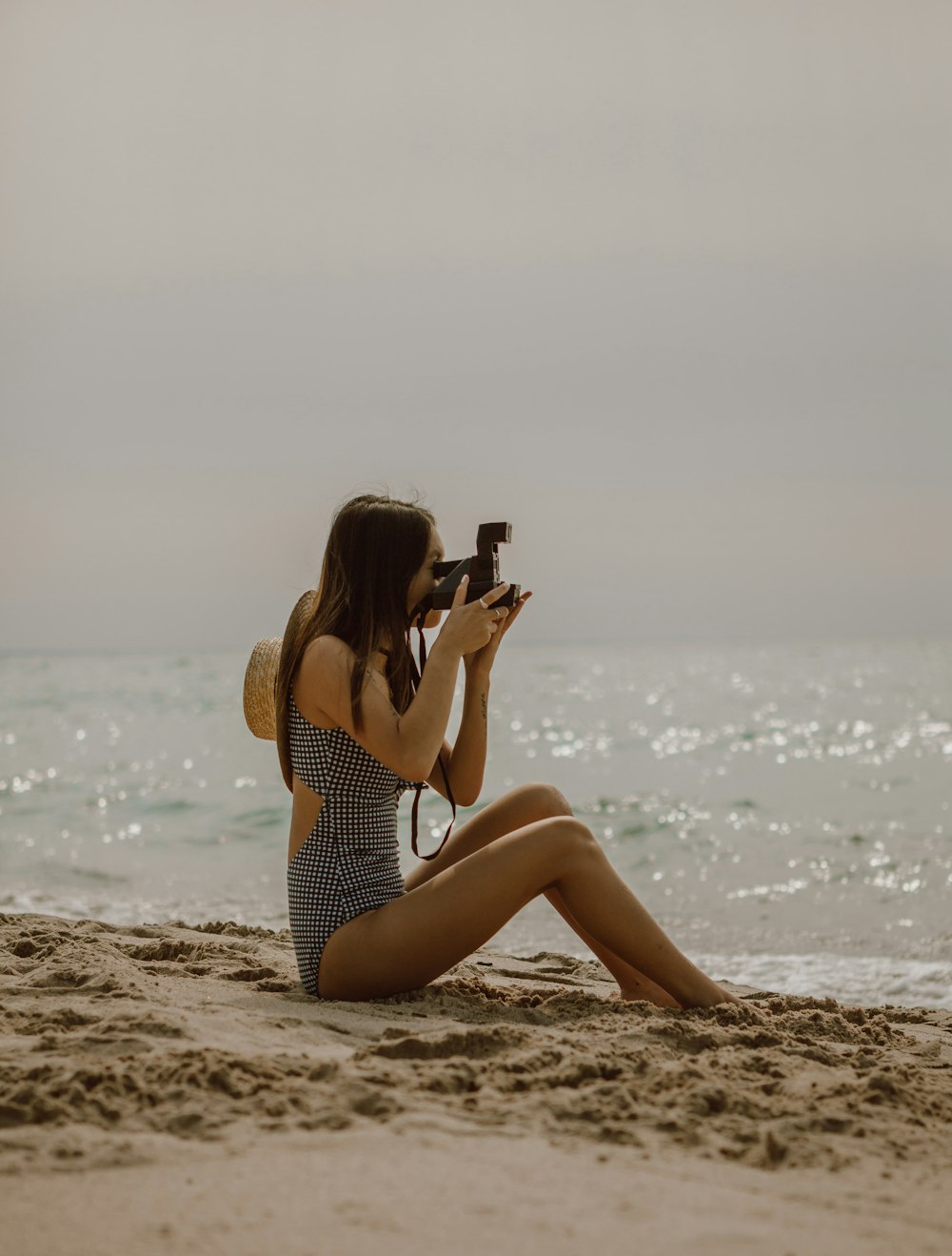 Mujer en traje de baño de lunares blanco y negro sentada en la orilla de la playa durante el día
