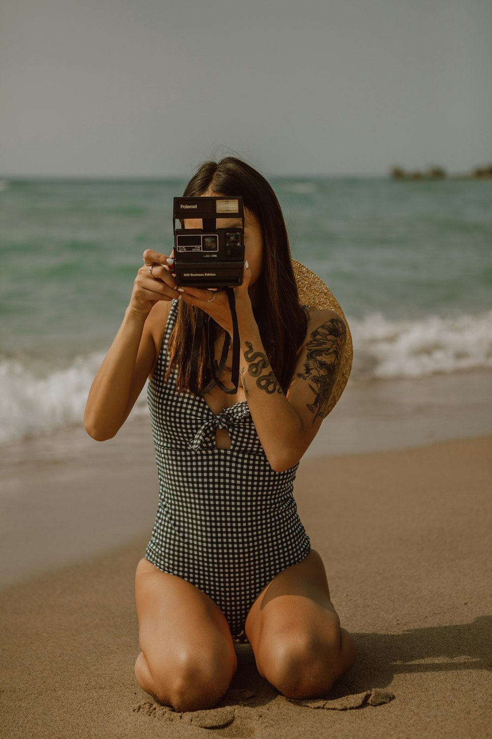 woman in black and white polka dot swimsuit holding black camera on beach during daytime