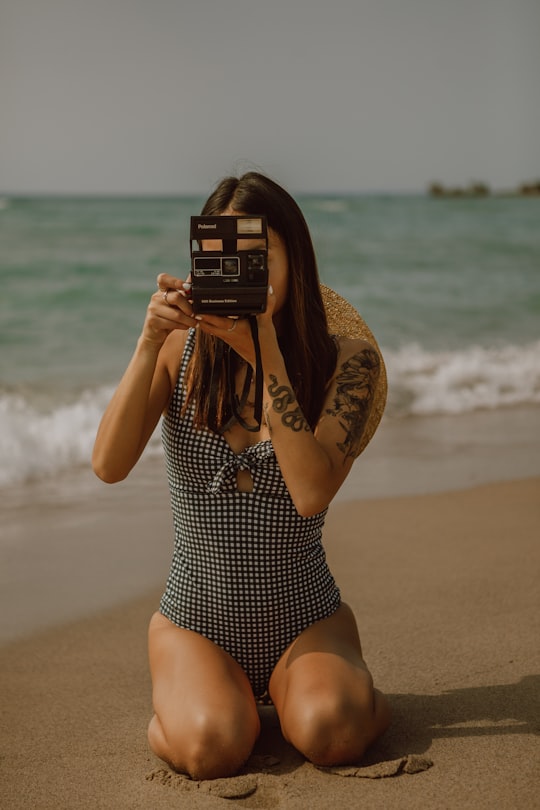 woman in black and white polka dot swimsuit holding black camera on beach during daytime in Tiny Canada