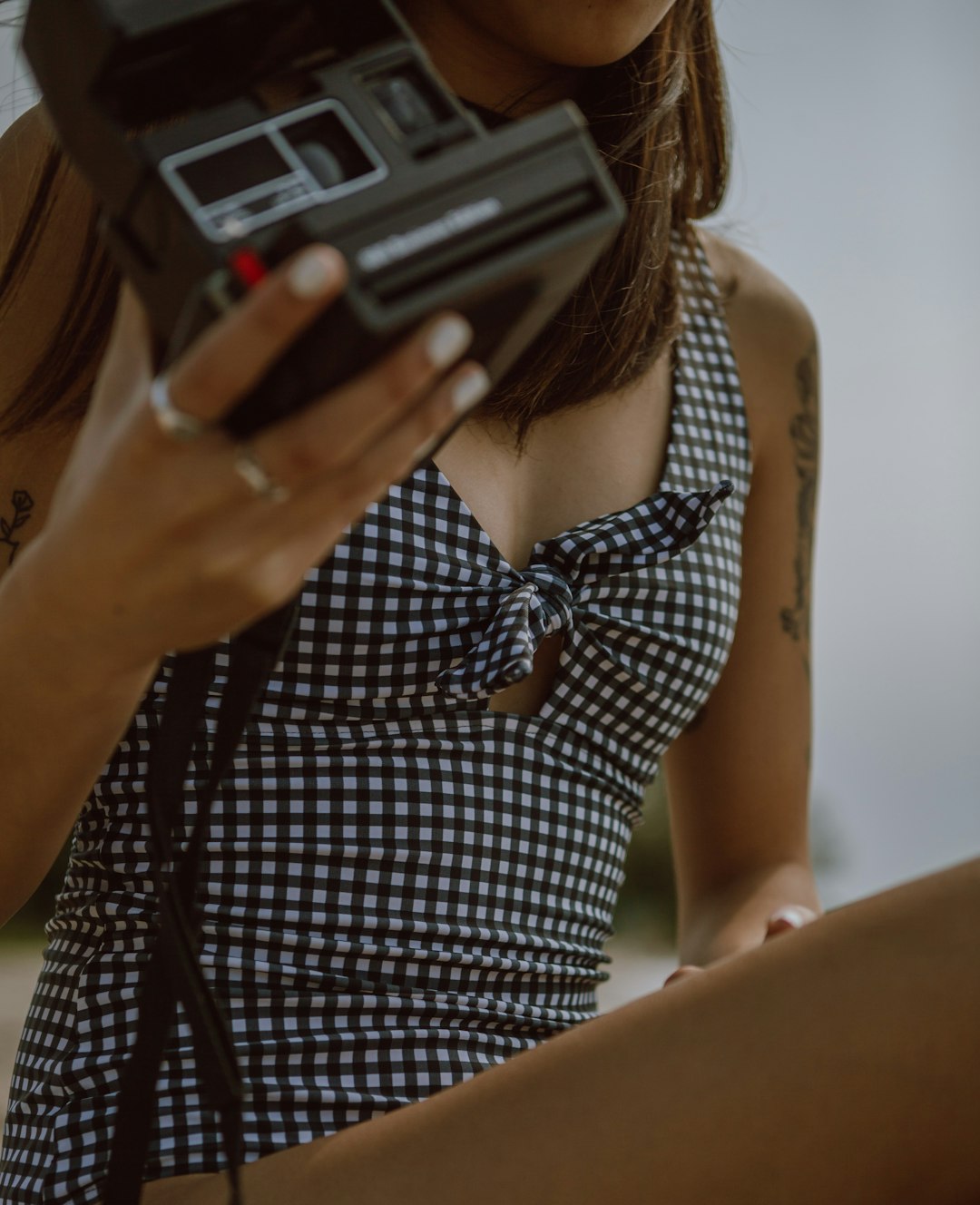 woman in black and white checkered sleeveless dress holding black and gray camera