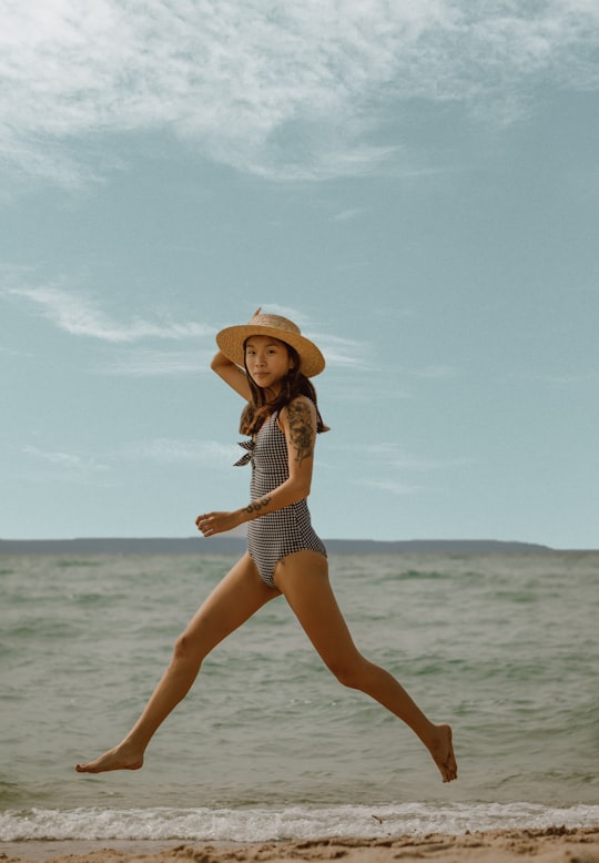 woman in white and black polka dot bikini wearing brown sun hat standing on beach during in Tiny Canada