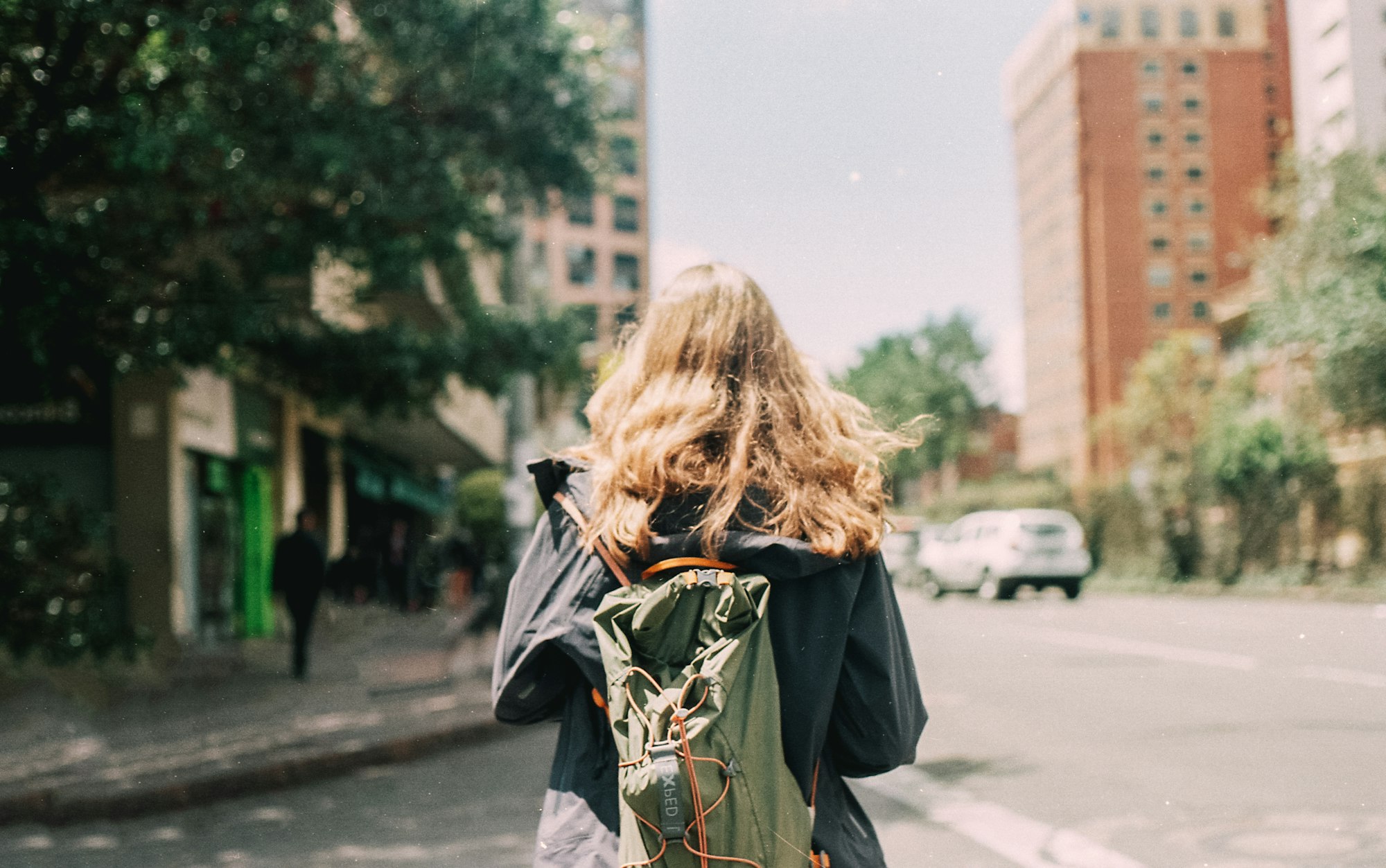 A woman in a black and yellow jacket walking on a sunlit sidewalk, captured on film with a Nikon FE and expired Agfa 35mm stock