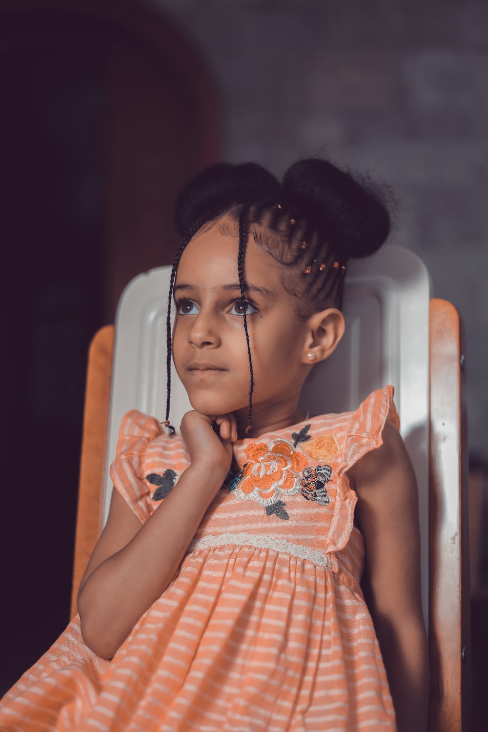 girl in orange and white dress sitting on white chair