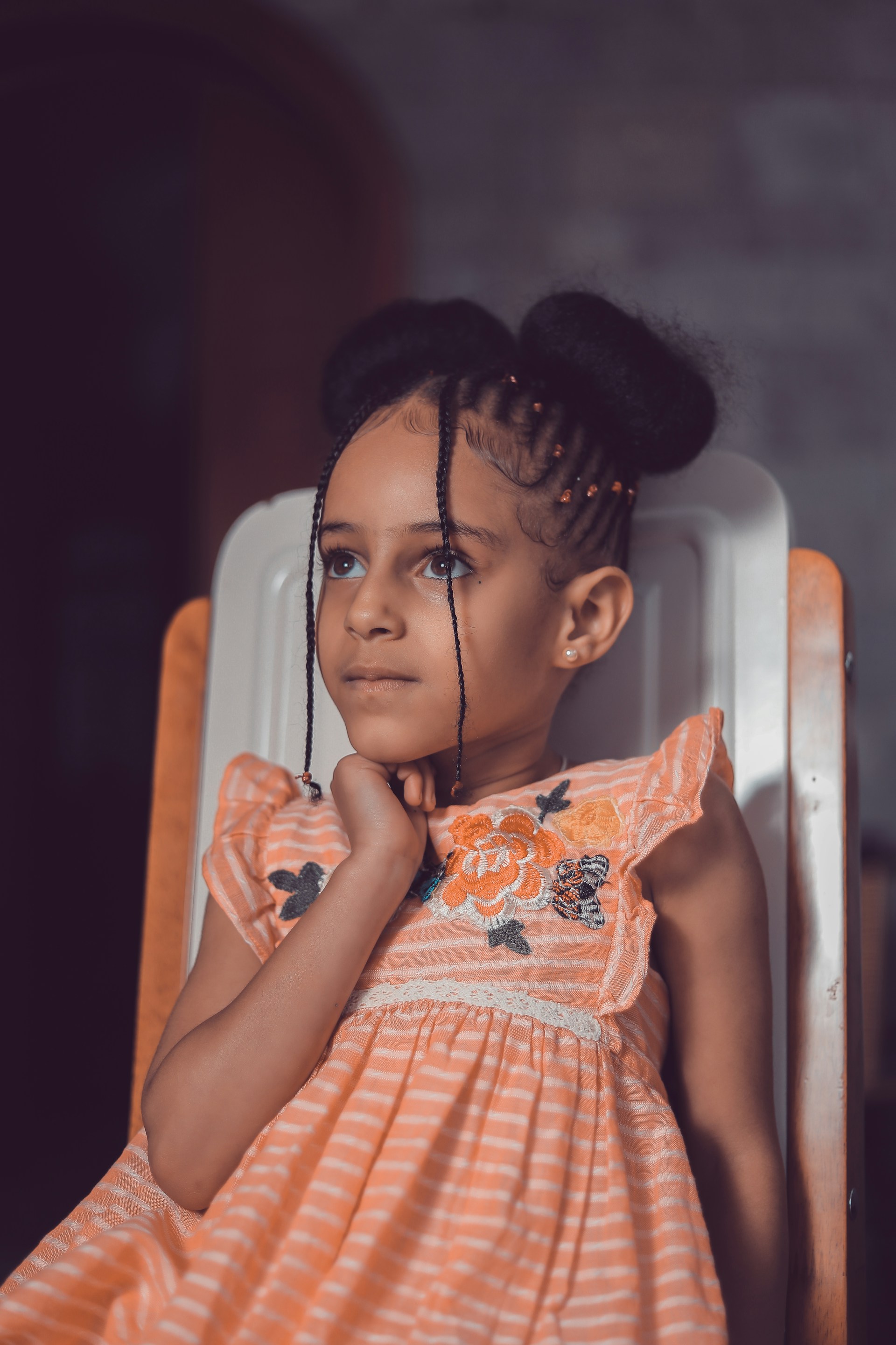 girl in orange and white dress sitting on white chair