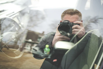 man in black jacket holding black nikon dslr camera