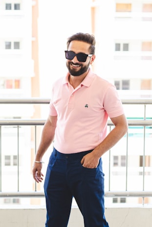 man in pink polo shirt and blue denim jeans wearing black sunglasses