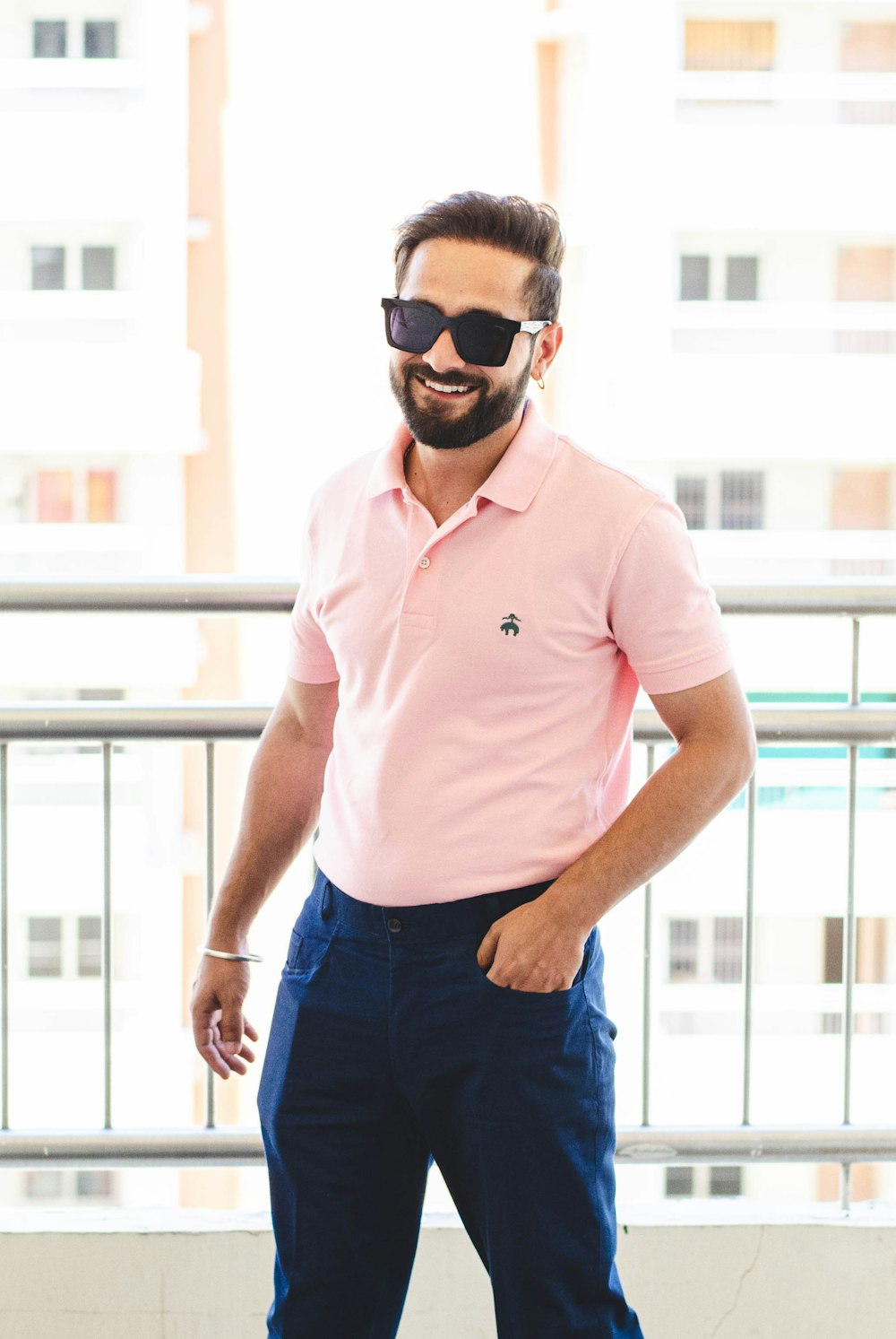 man in pink polo shirt and blue denim jeans wearing black sunglasses