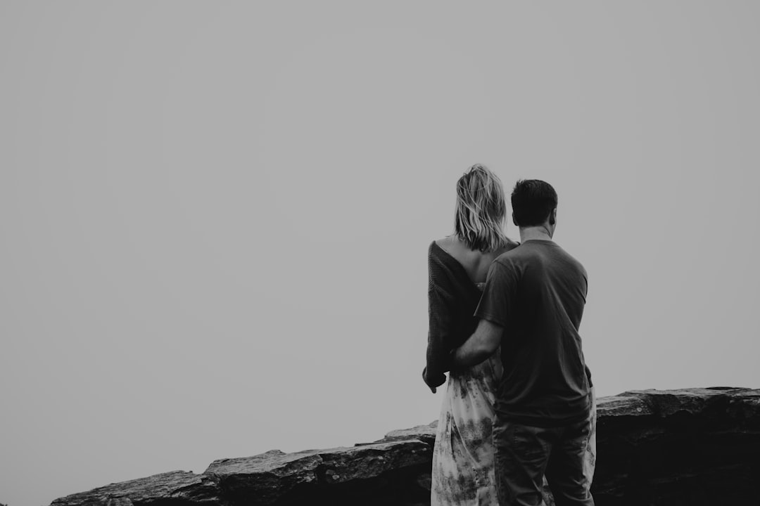 man and woman standing on rock formation in grayscale photography