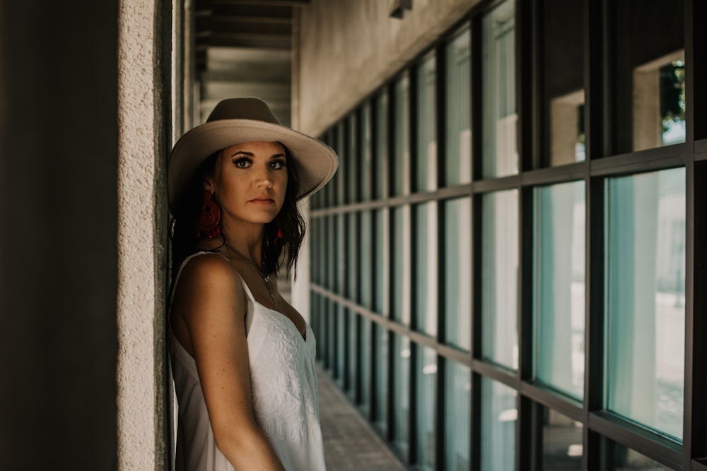 woman in white spaghetti strap dress wearing brown hat standing in front of blue metal gate