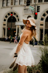 A cheerful woman wearing a flowing summer dress, smiling in a sunlit urban street.